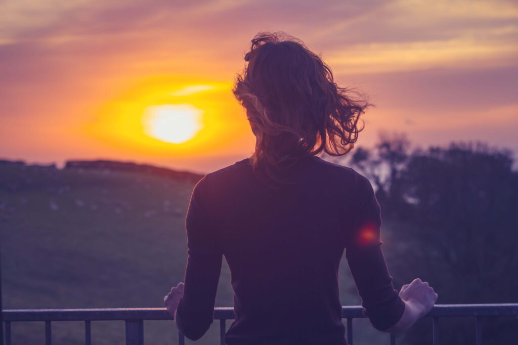Eine Frau steht souverän und klar und sieht in den Sonnenuntergang