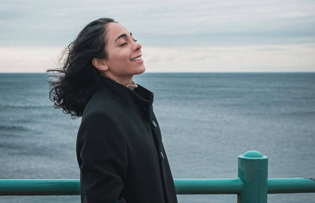 #68 ziemlichglücklich Beitragsbild: Eine Frau steht glücklich und befreit am Meer