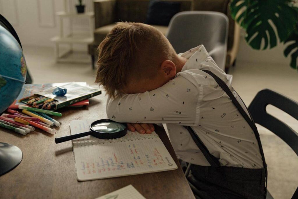 #100 ziemlichglücklich Beitragsbild: Ein Schüler liegt unmotiviert auf seinen Hausaufgaben