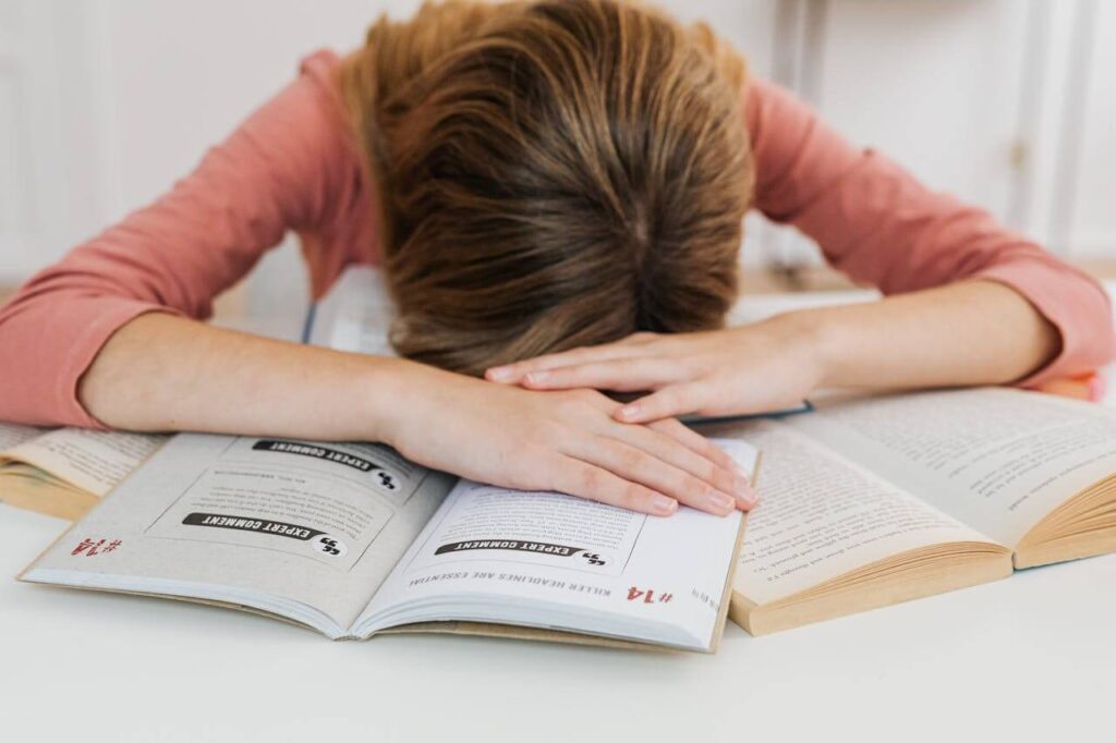 #96 ziemlichglücklich Beitragsbild: Eine Schülerin liegt unmotiviert über Schulbüchern